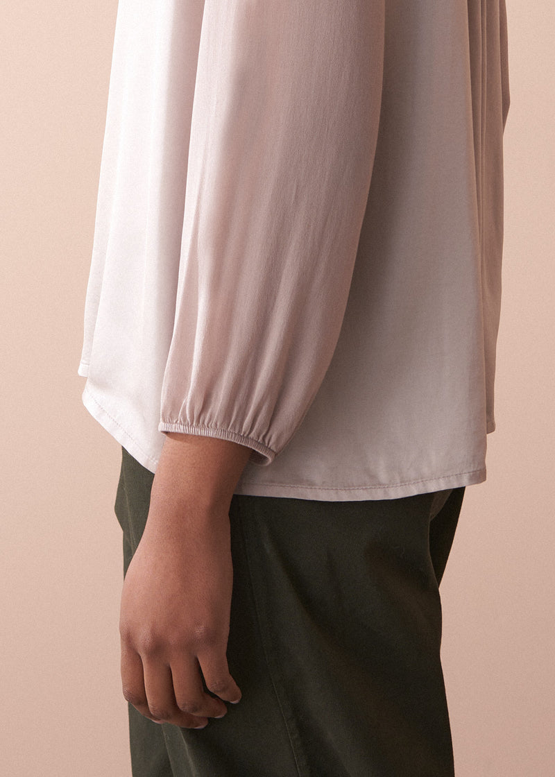Person wearing a pale lilac satin  blouse with long sleeves against a beige background