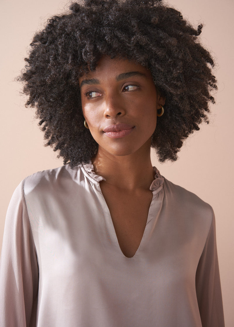 Woman with an afro wearing a pale lilac satin  blouse against a beige background