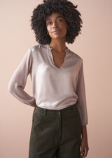 Woman wearing a pale lilac satin  blouse and dark green pants against a beige background