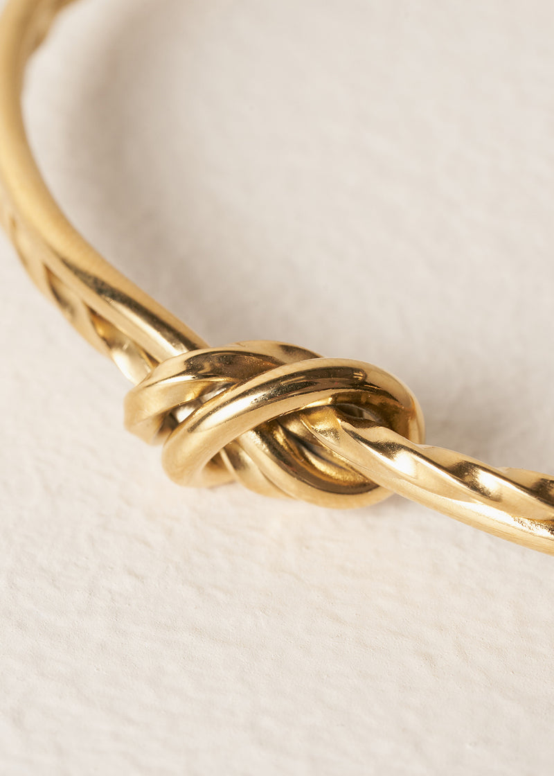 Gold bracelet with a knot design on a light beige background