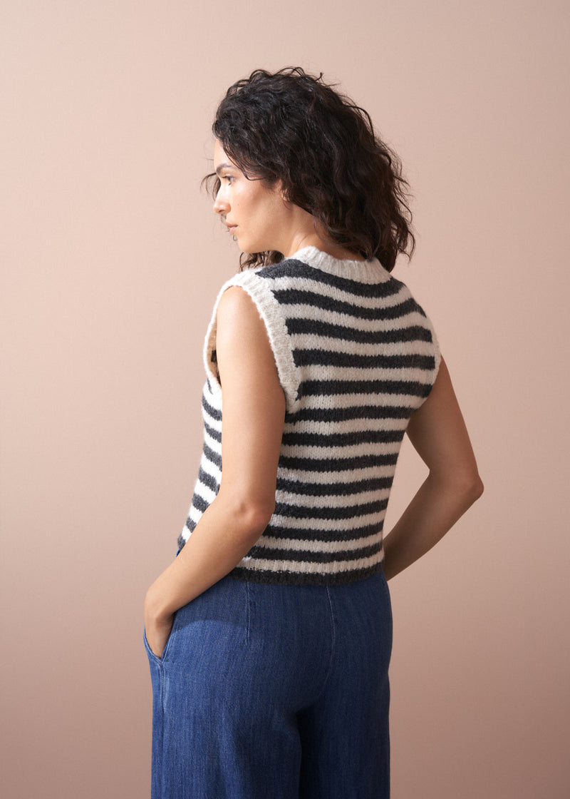 Woman wearing a black and white striped sleeveless sweater against a beige background