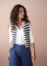Woman wearing a striped cardigan, white shirt, and blue pants against a beige background