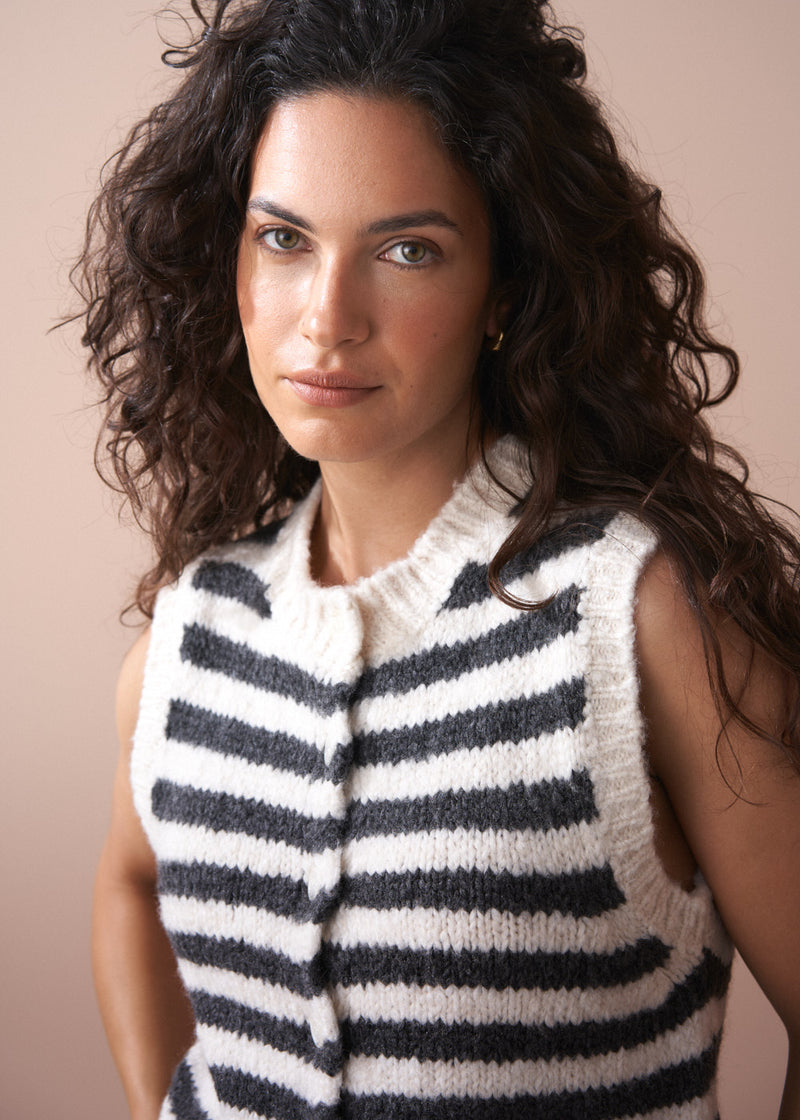 Woman wearing a black and white striped sleeveless knitted vest against a beige background