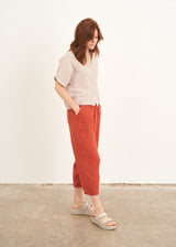 A model wearing a blush pink cropped linen shirt with a pair of rust coloured cropped trousers and off white slides