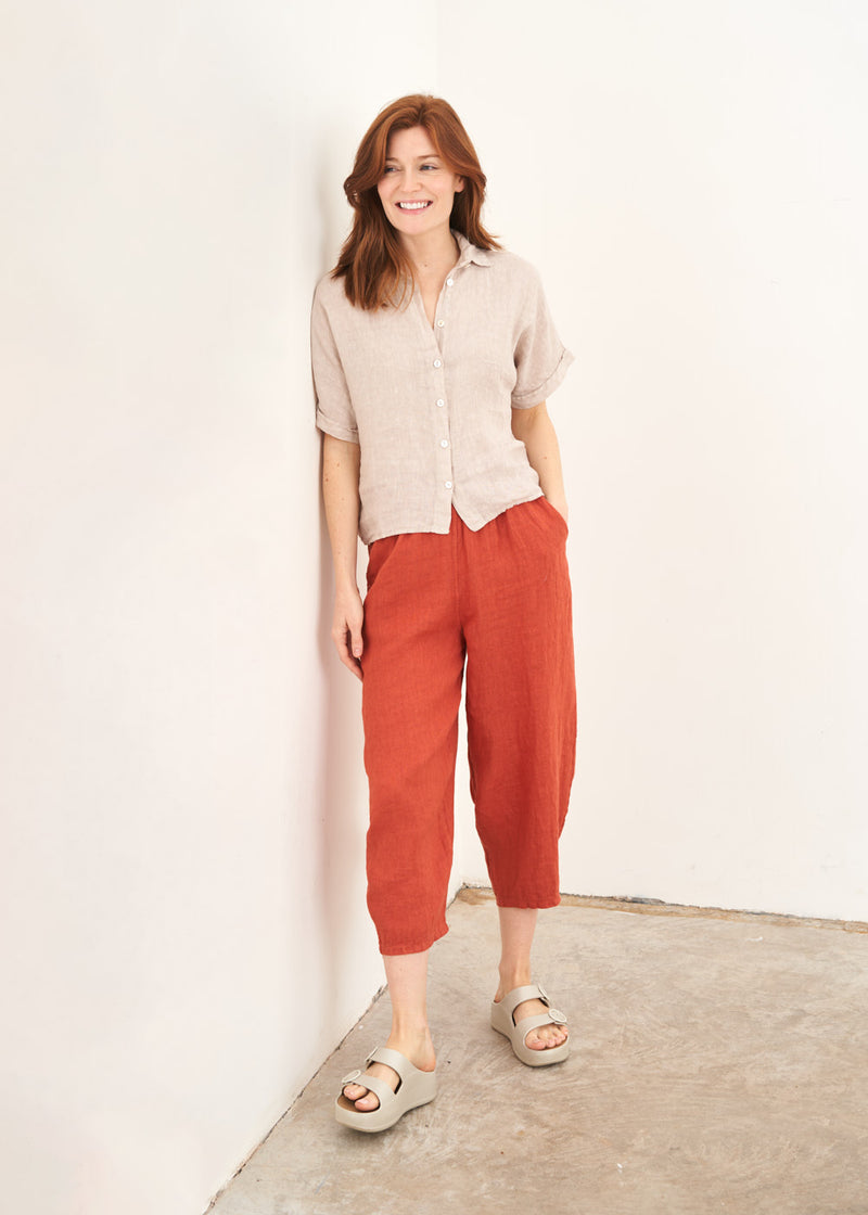 A model wearing a blush pink cropped linen shirt with a pair of rust coloured cropped trousers and off white slides