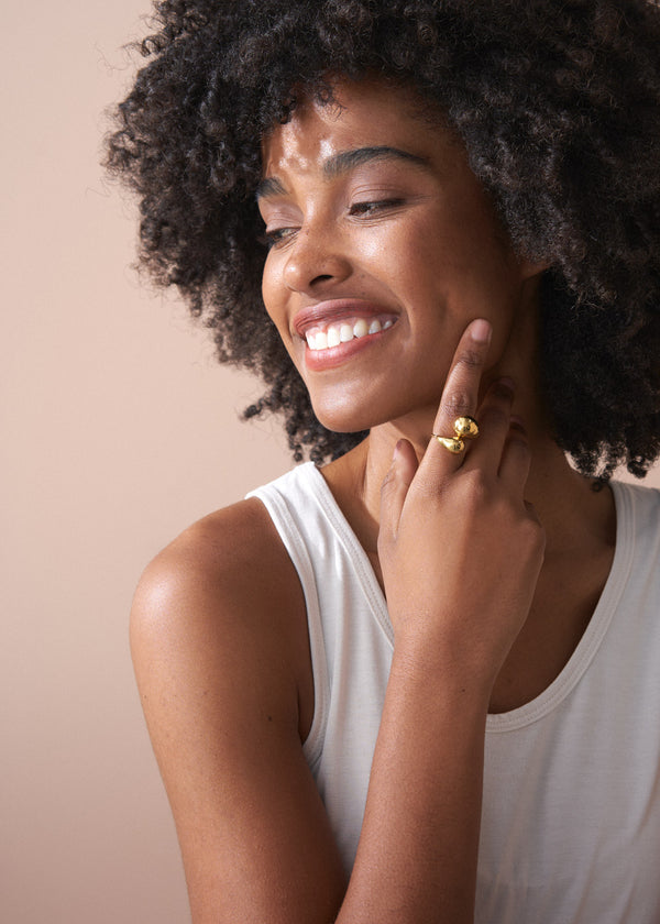 Woman with a gold ring on her finger against a beige background