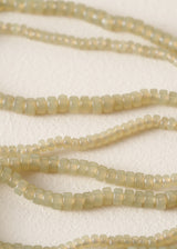 Close-up of pale yellow-beige cylindrical beads strung on cords, arranged in curved lines on a textured off-white background.