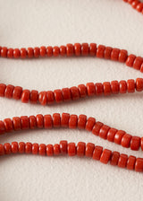 Close-up of red cylindrical beads strung on cords, arranged in curved lines on a light beige textured background.