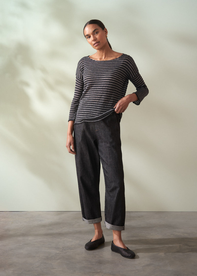 Woman wearing a striped sweater and dark pants against a plain background