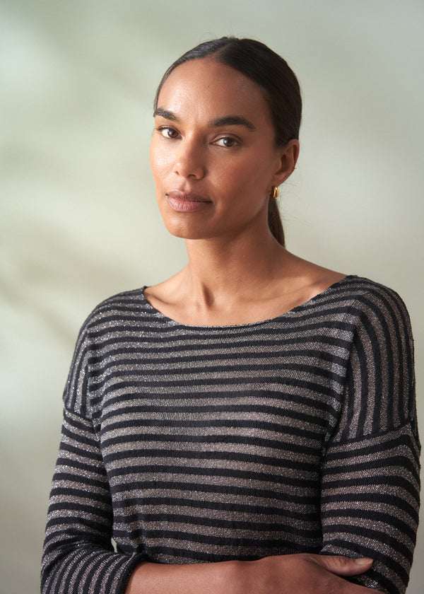 Woman wearing a black and silver striped long sleeve top against a plain background