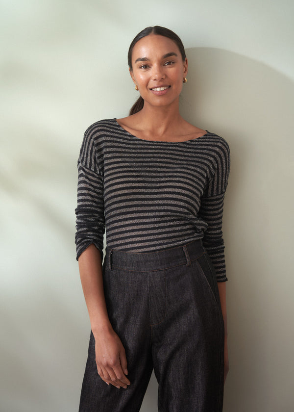Woman wearing a black and silver striped top and dark jeans against a plain background