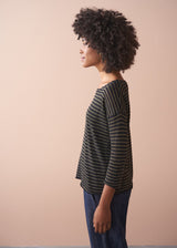 Woman wearing a striped gold and black top against a beige background