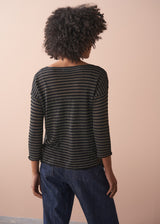 Woman wearing a striped gold and black top against a beige background