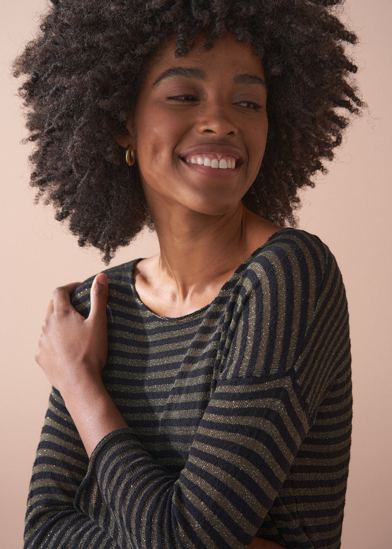Woman wearing a striped gold and black top against a beige background