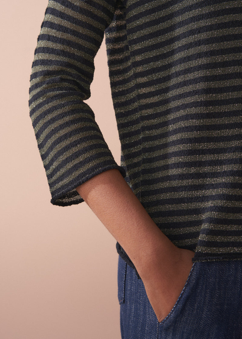 Woman wearing a striped gold and black top against a beige background