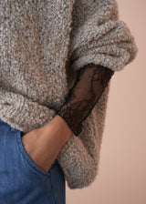 Close-up of a person wearing a textured sweater with a visible lace sleeve against a beige background