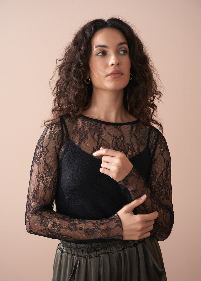 Woman wearing a black lace top against a beige background