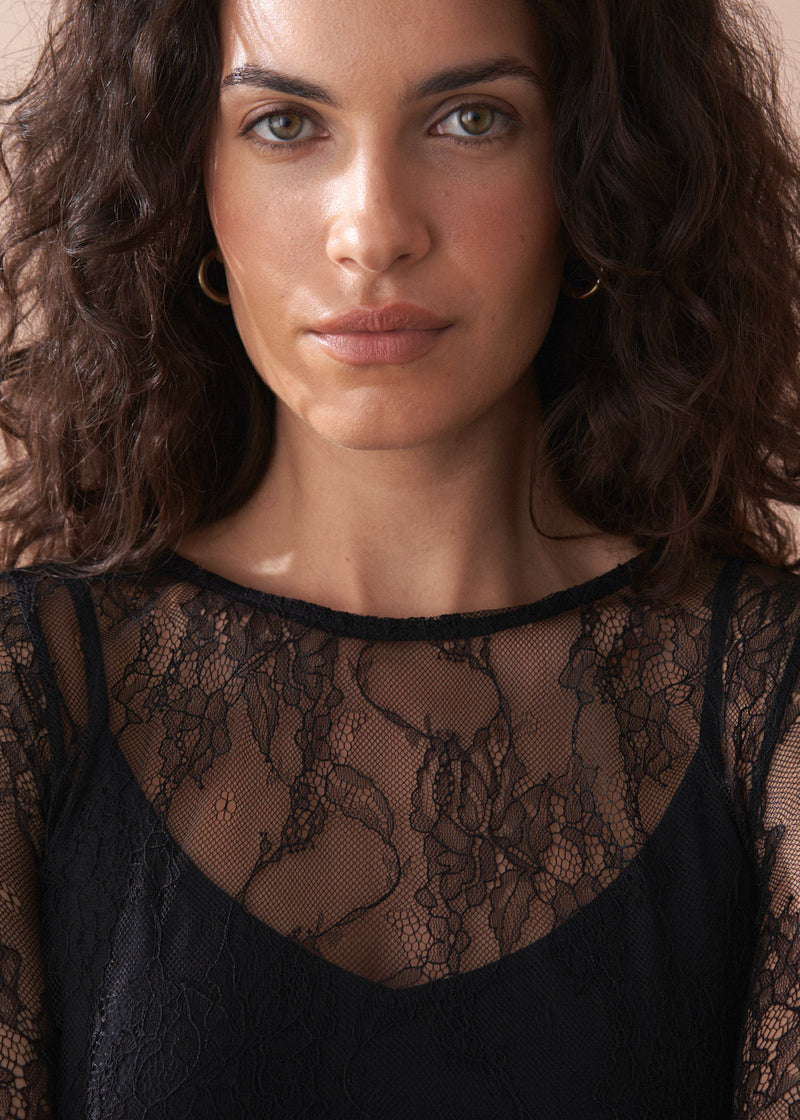 Woman wearing a black lace top against a neutral background