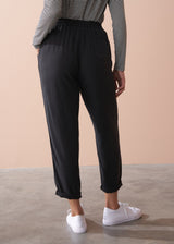 Woman wearing a striped long sleeve shirt and black drawstring trousers against a beige background