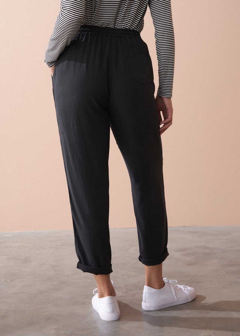 Woman wearing a striped long sleeve shirt and black drawstring trousers against a beige background