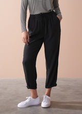 Woman wearing a striped long sleeve shirt and black drawstring trousers against a beige background