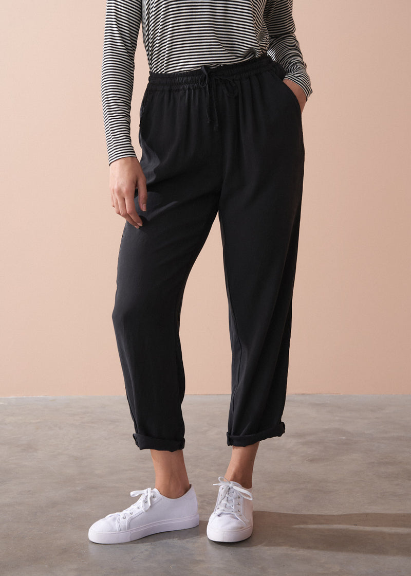 Woman wearing a striped long sleeve shirt and black drawstring trousers against a beige background