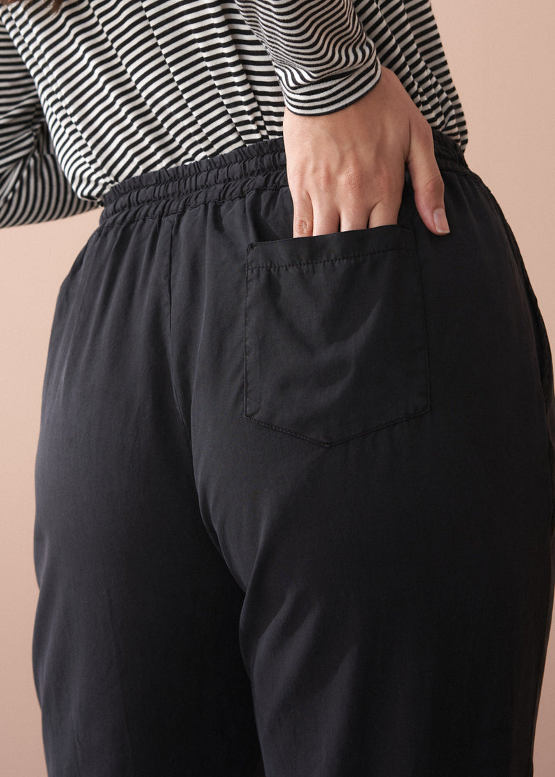 Woman wearing a striped long sleeve shirt and black drawstring trousers against a beige background