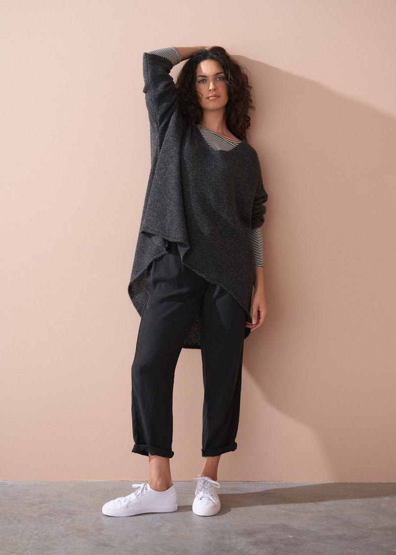 Woman wearing a striped long sleeve shirt and black drawstring trousers against a beige background