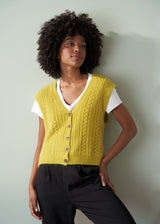 Woman wearing an acid yellow cable knit vest over a white shirt against a plain background