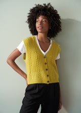 Woman wearing an acid yellow cable knit vest over a white shirt against a plain background