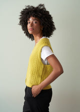 Woman wearing an acid yellow cable knit vest over a white shirt against a plain background