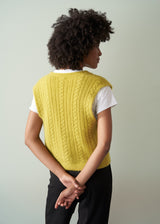 Woman wearing an acid yellow cable knit vest over a white shirt against a plain background