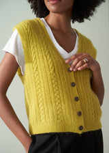 Woman wearing an acid yellow cable knit vest over a white shirt against a plain background