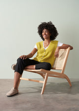 Woman wearing an acid yellow cable knit vest over a white shirt against a plain background