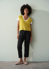 Woman wearing an acid yellow cable knit vest over a white shirt against a plain background