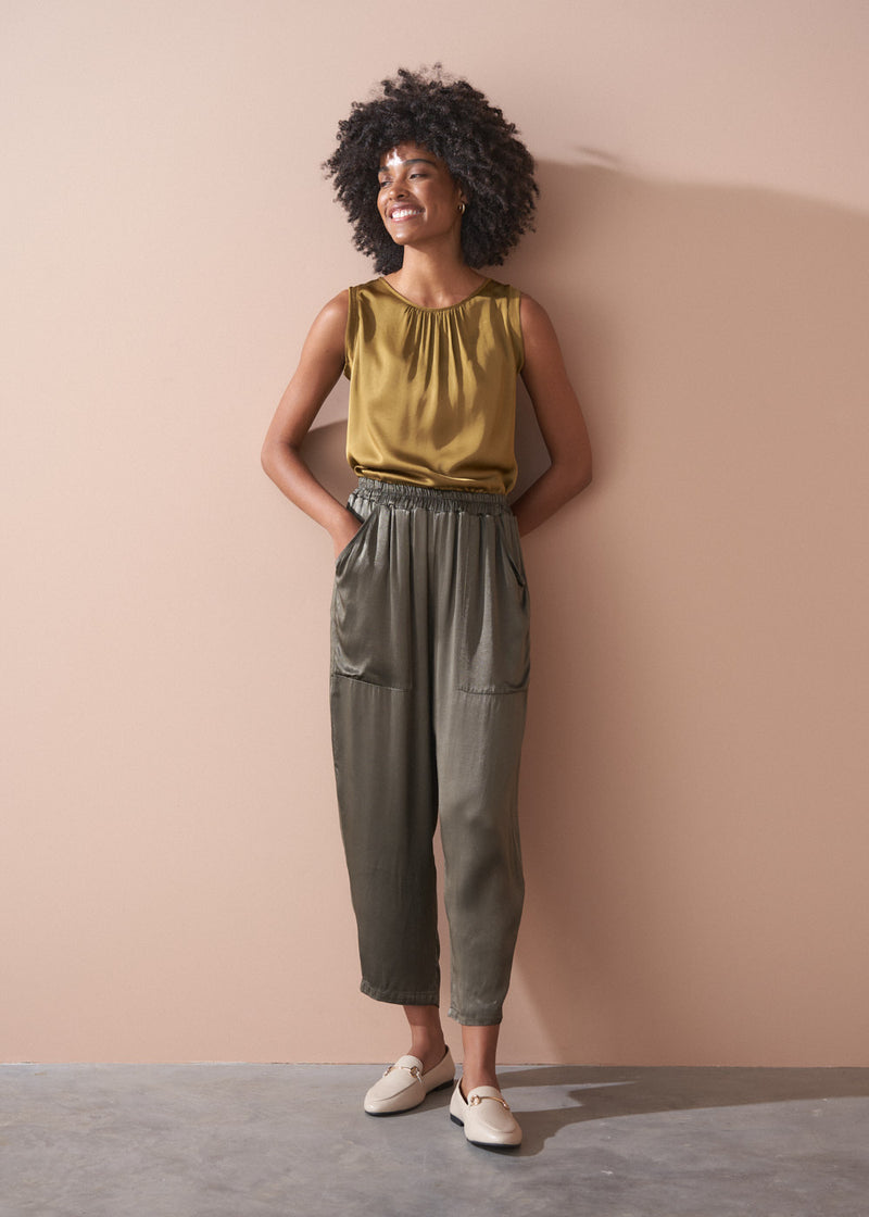 Woman wearing a gold satin top and green satin trousers against a beige wall