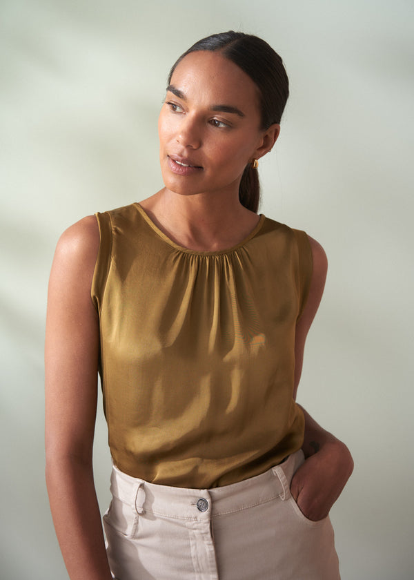 Woman wearing an olive green sleeveless satin top against a plain background