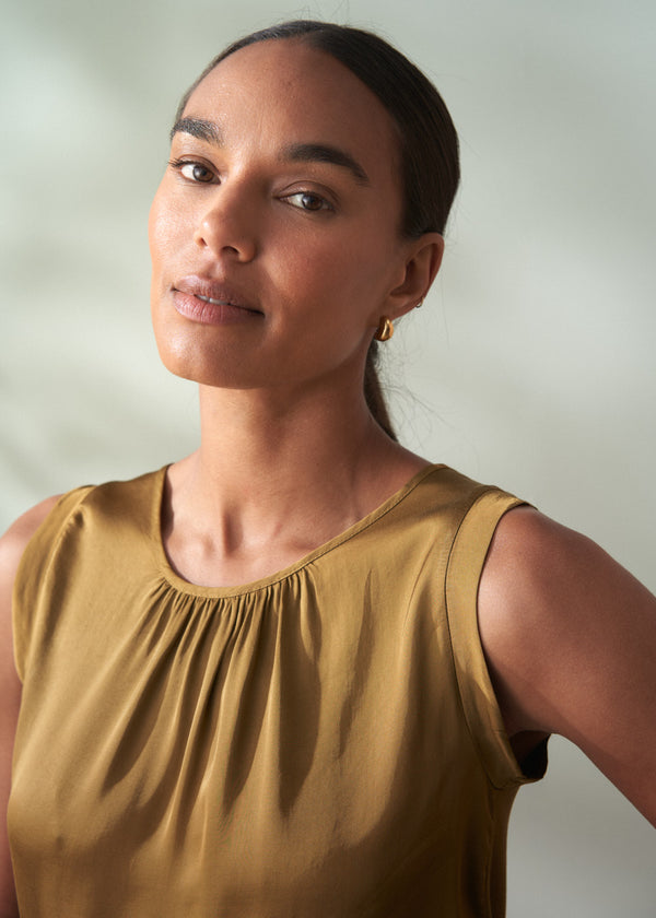 Woman wearing an olive green sleeveless satin top against a plain background