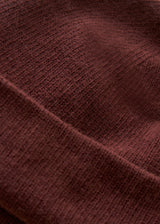 Close-up of a ribbed knit fabric in a deep burgundy or maroon color, showing the texture and folds of the material.
