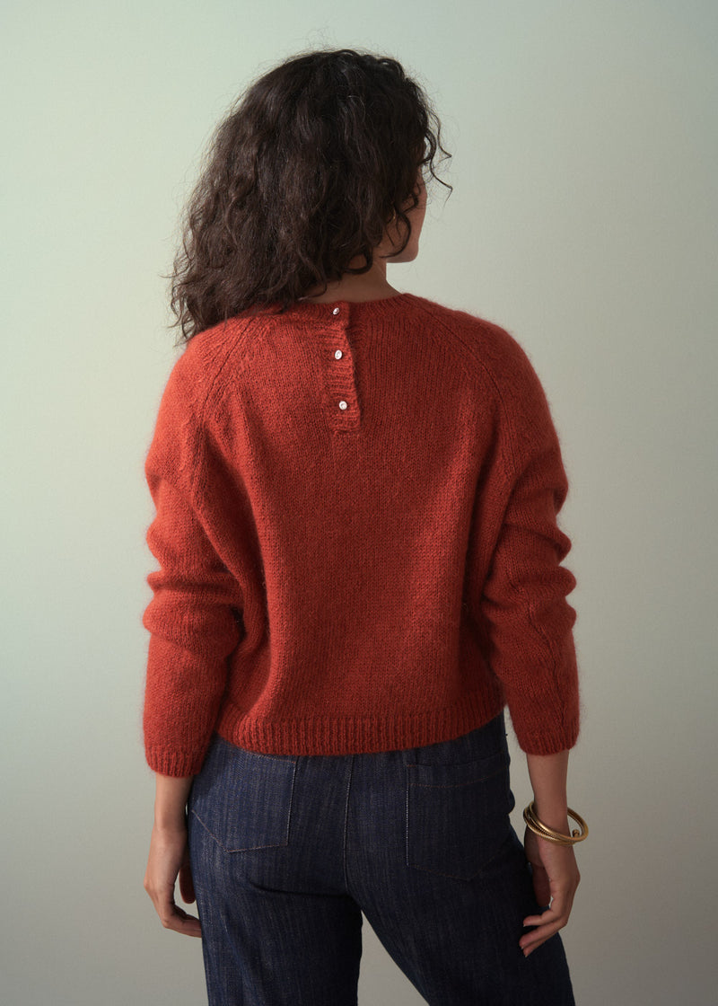 Person wearing a red sweater with buttons, standing against a plain background