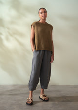 Woman wearing a khaki green sleeveless sweater and checkered pants against a neutral background