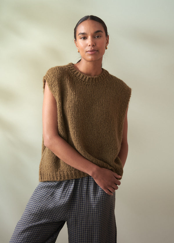 Woman wearing a khaki green knitted vest against a plain background