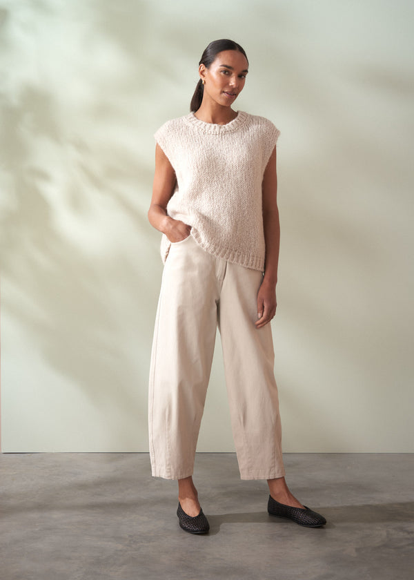 Woman wearing a light pink sleeveless top and beige trousers against a neutral background