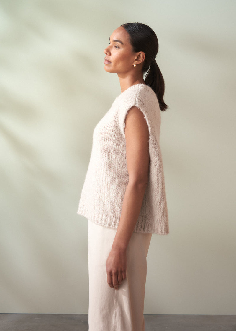 Woman wearing a textured beige top and light-colored trousers against a plain background