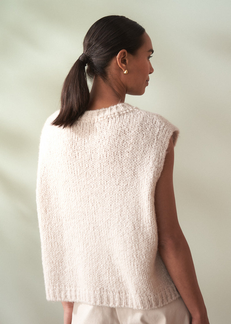 Woman wearing a beige knitted vest against a plain background