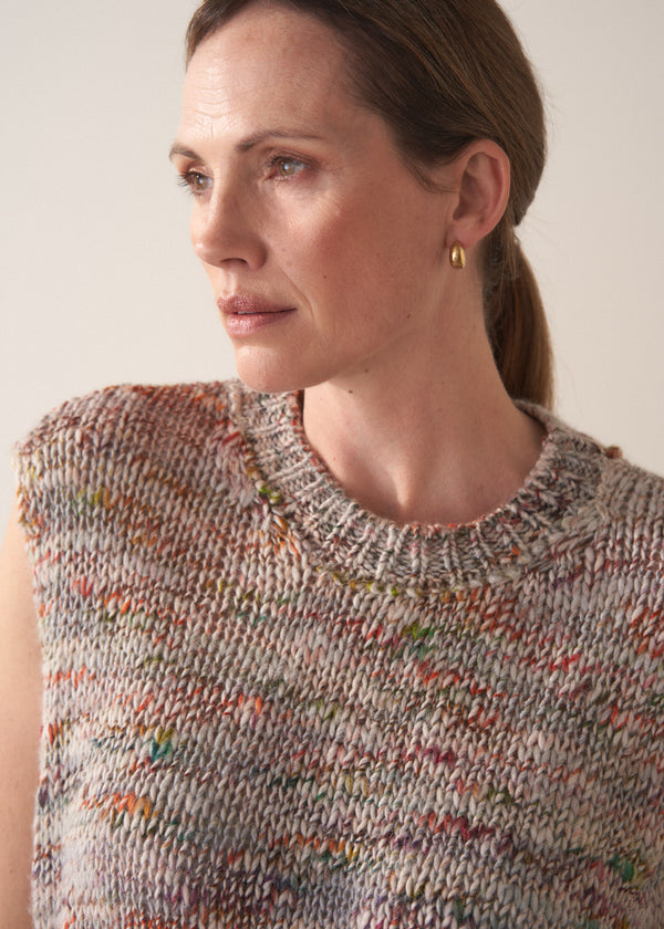 Woman wearing a sleeveless, multicolored space dye knit sweater against a plain background