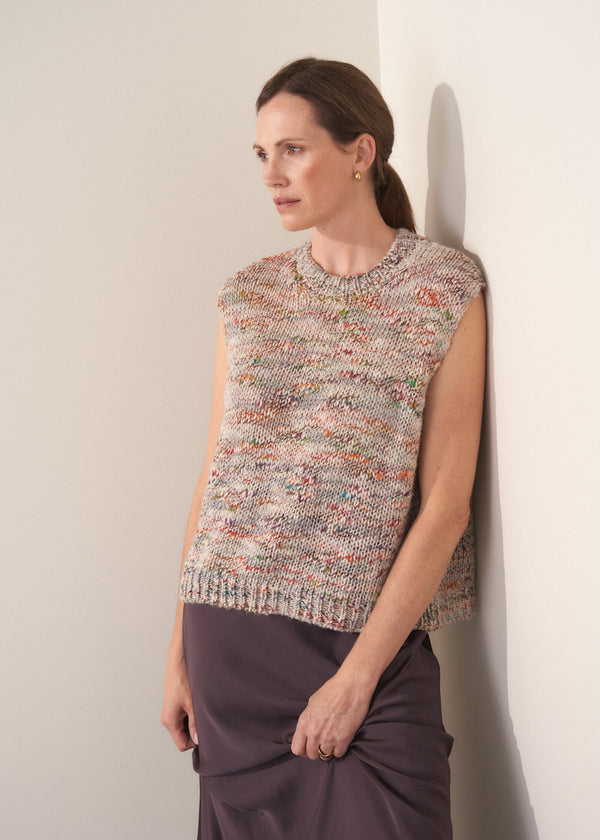 Woman wearing a sleeveless, multicolored space dye knit sweater against a plain background