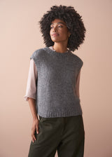 Woman wearing a grey sleeveless sparkle sweater against a beige background