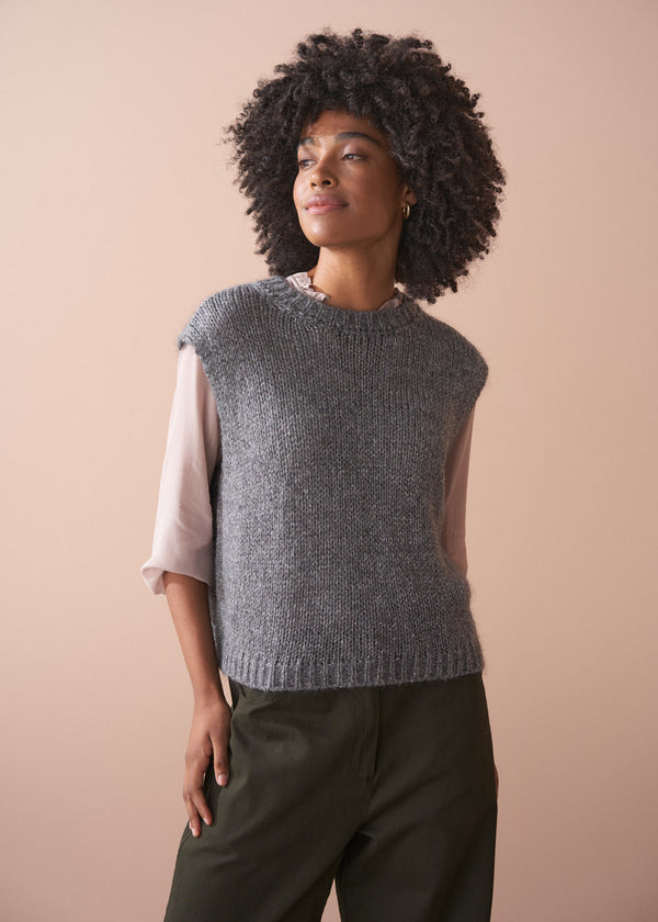 Woman wearing a grey sleeveless sparkle sweater against a beige background