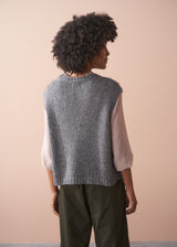 Woman wearing a grey sleeveless sparkle sweater against a beige background